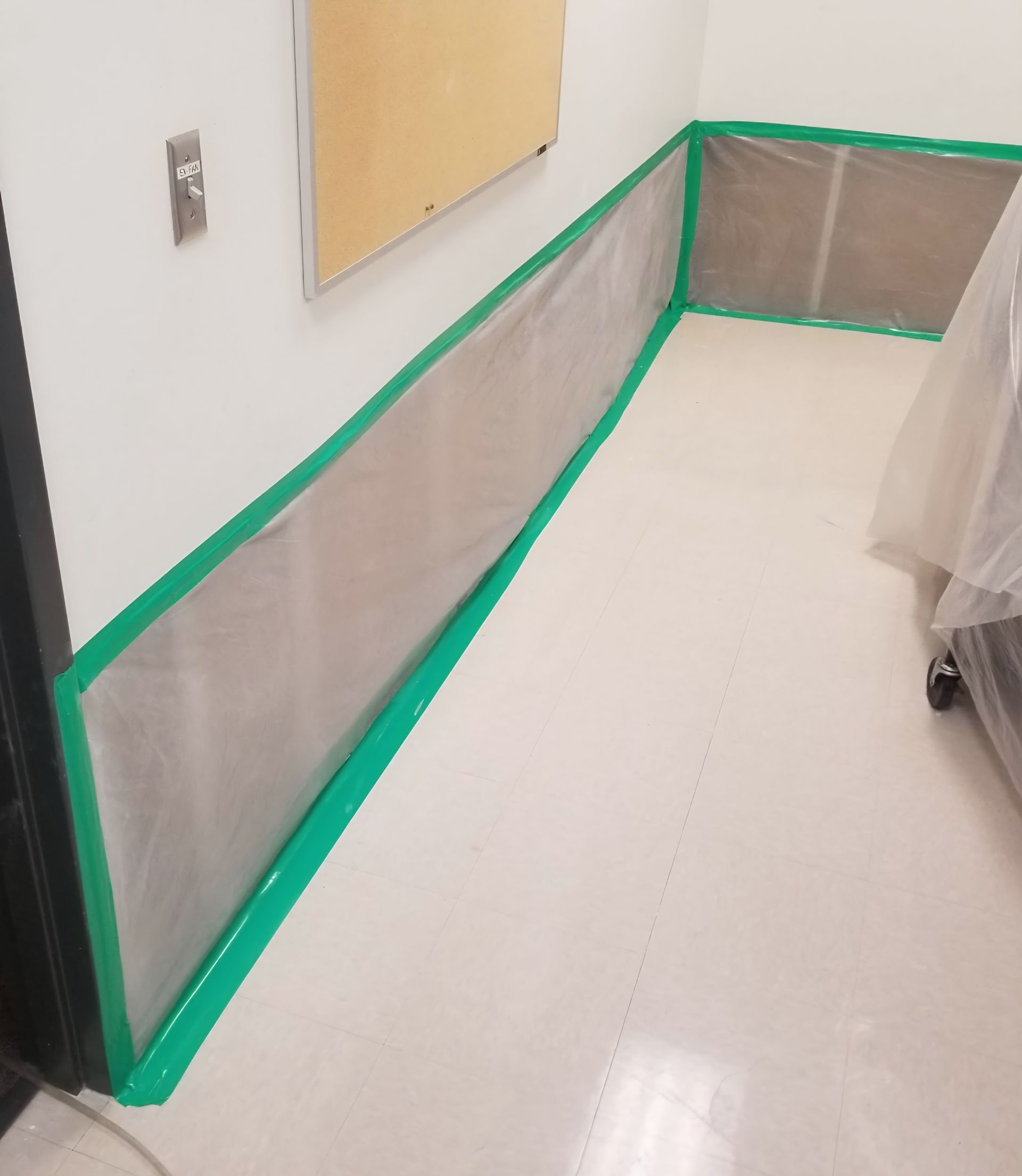 White room with green-taped plastic barrier along walls and floor.