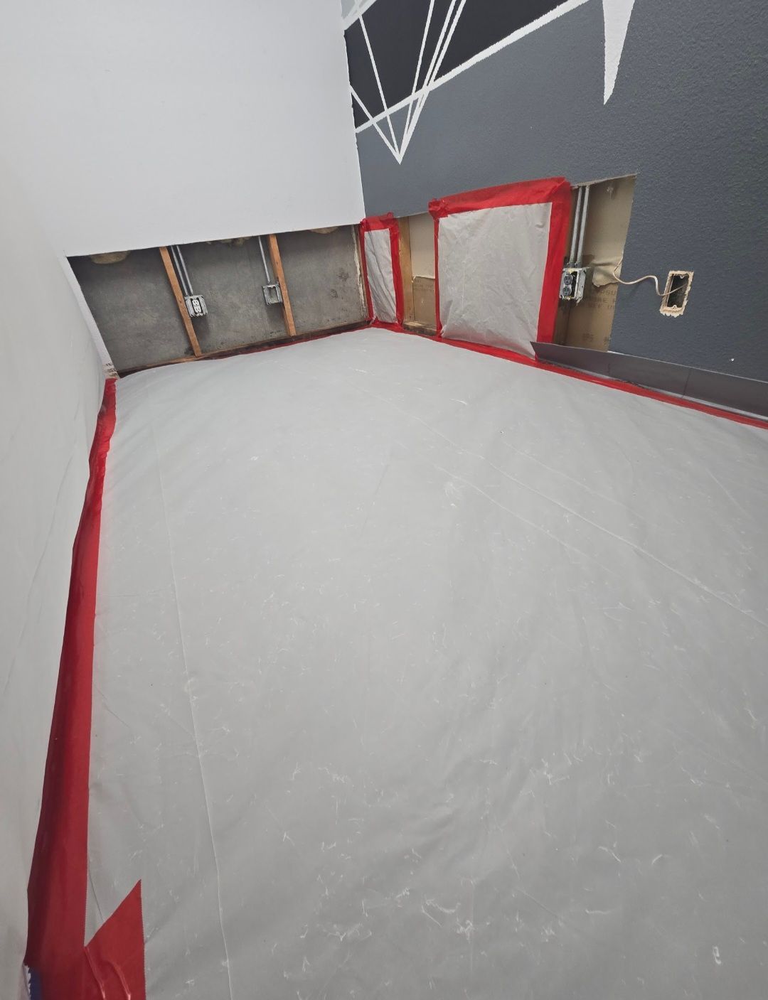 Room under construction, covered in plastic sheeting, with exposed wall studs and electrical outlets. Red tape visible.