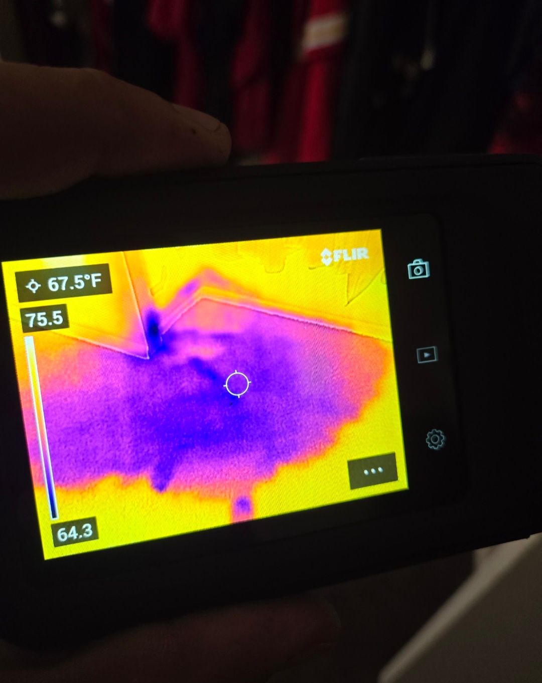 Thermal camera view showing a dark, cold area surrounded by warmer yellow/orange, held by a hand.