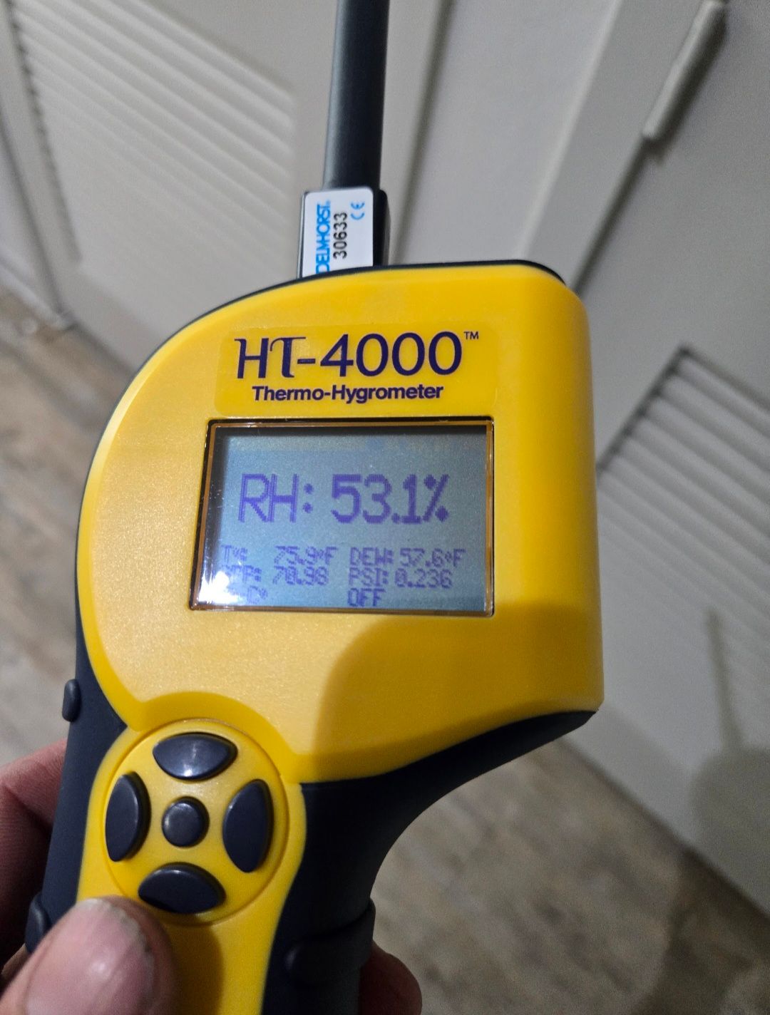 Yellow and black HT-4000 Thermo-Hygrometer displays 53.1% relative humidity. Hand holding the device near a white surface.