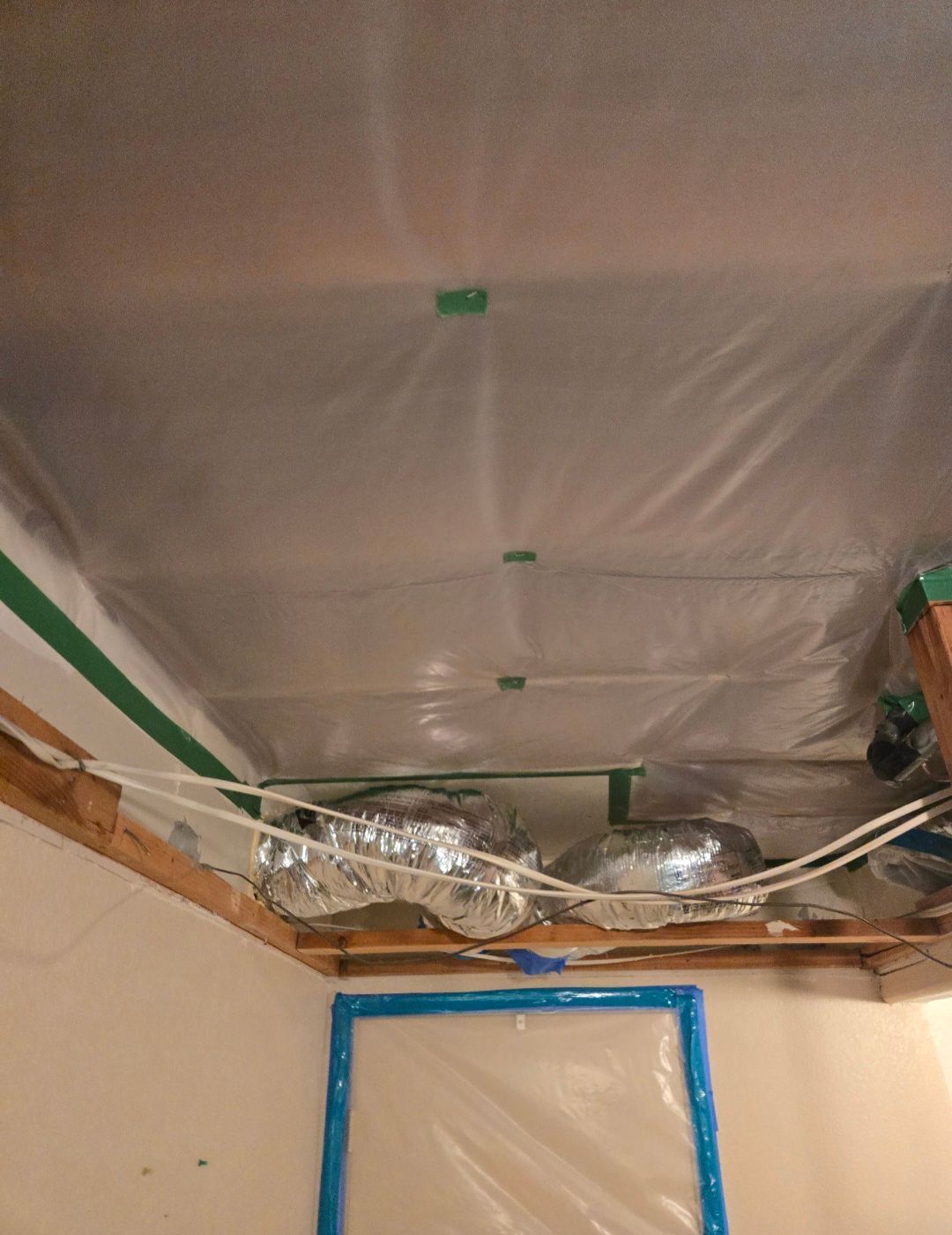 Ceiling with plastic sheeting, HVAC ducts, and masking tape.