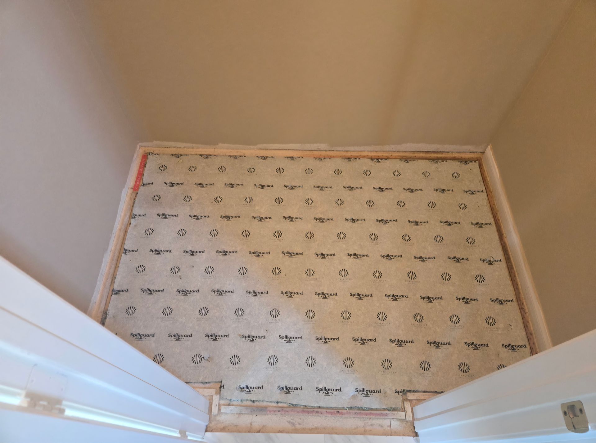 View from above of a room with beige walls, doorway, and light-colored padding in the center, ready for flooring.