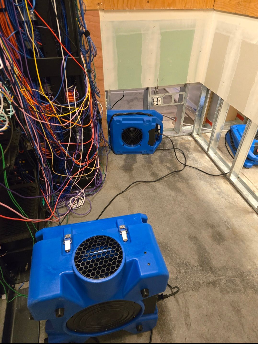 Blue air movers in a flooded room with exposed wiring and unfinished walls.