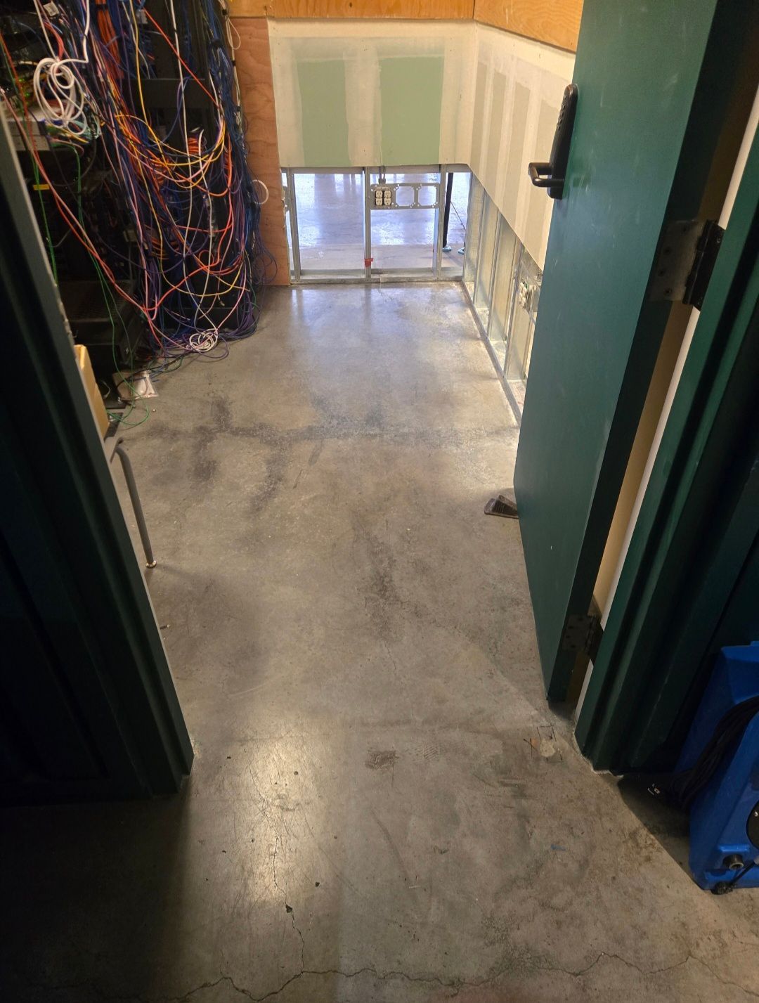 View down a concrete hallway with open doors, leading to a lower level. Wire bundles on the left.