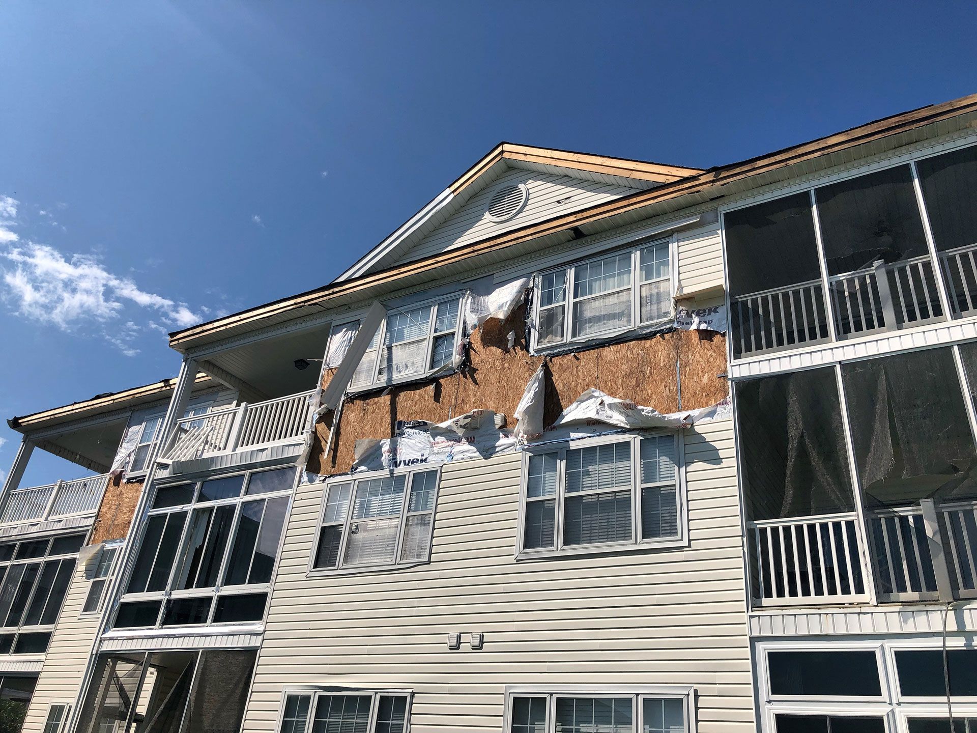 Building with damaged siding and exposed wood under a blue sky.