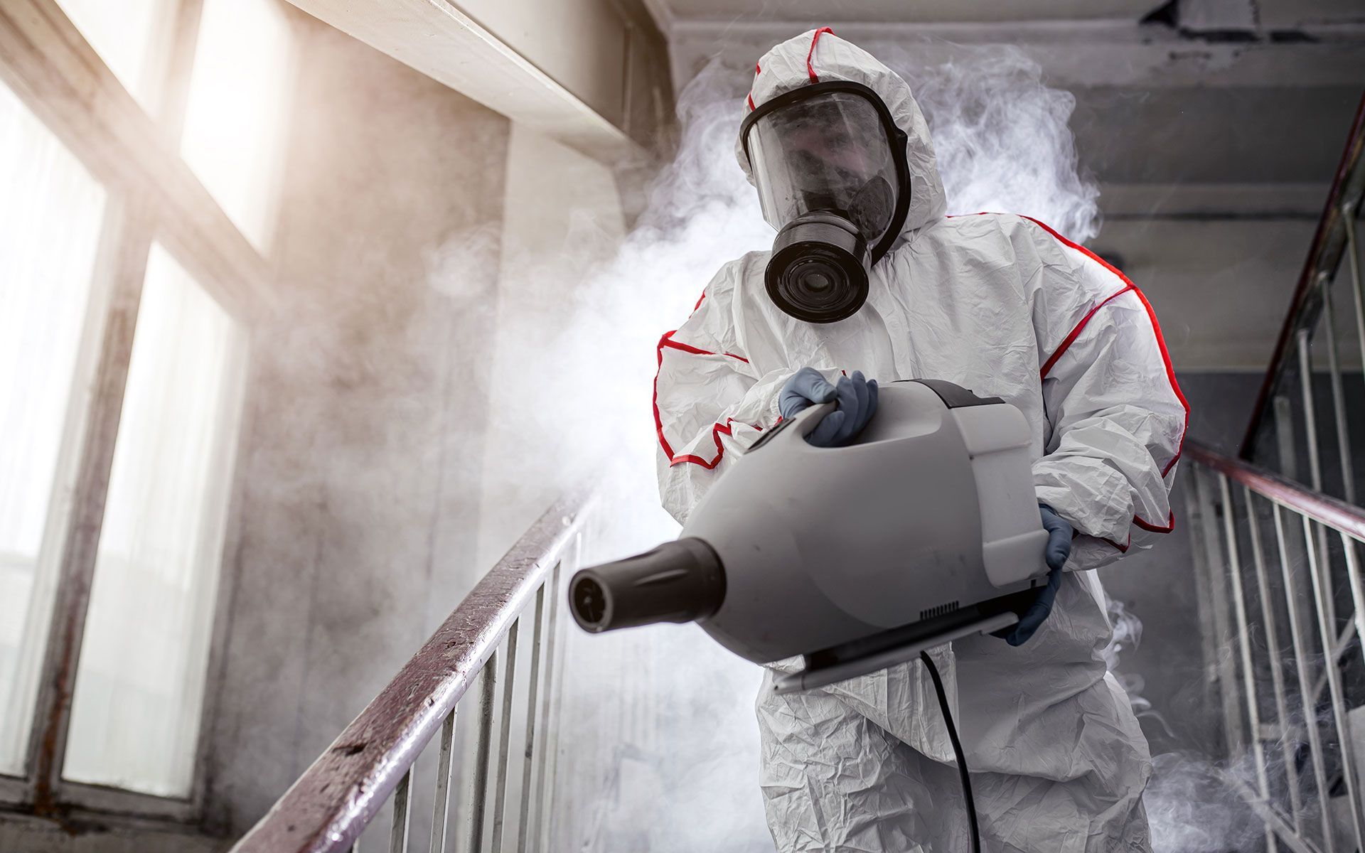 Person in hazmat suit spraying disinfectant on stairs.