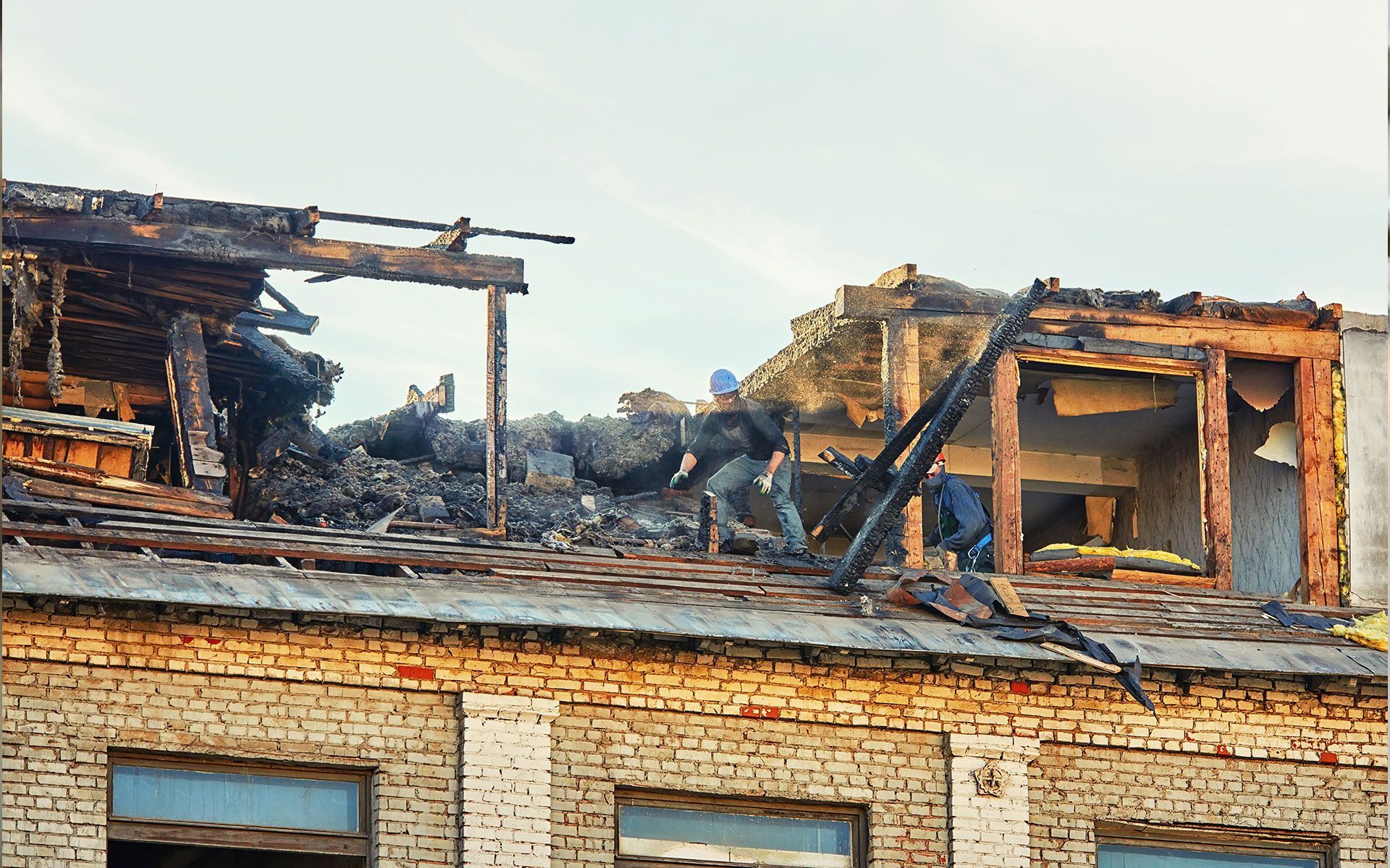 Building roof destroyed by fire; people on the roof. Brick facade.