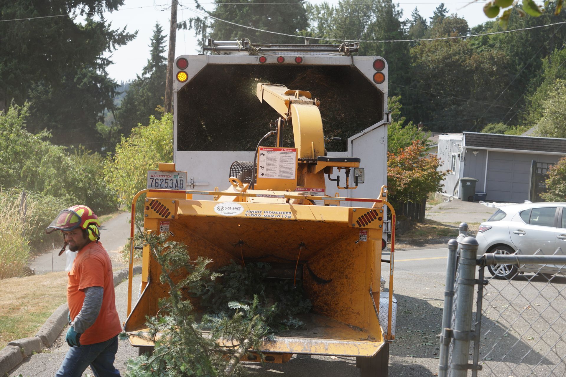 Man feeding branches into a wood chipper truck on a residential street.