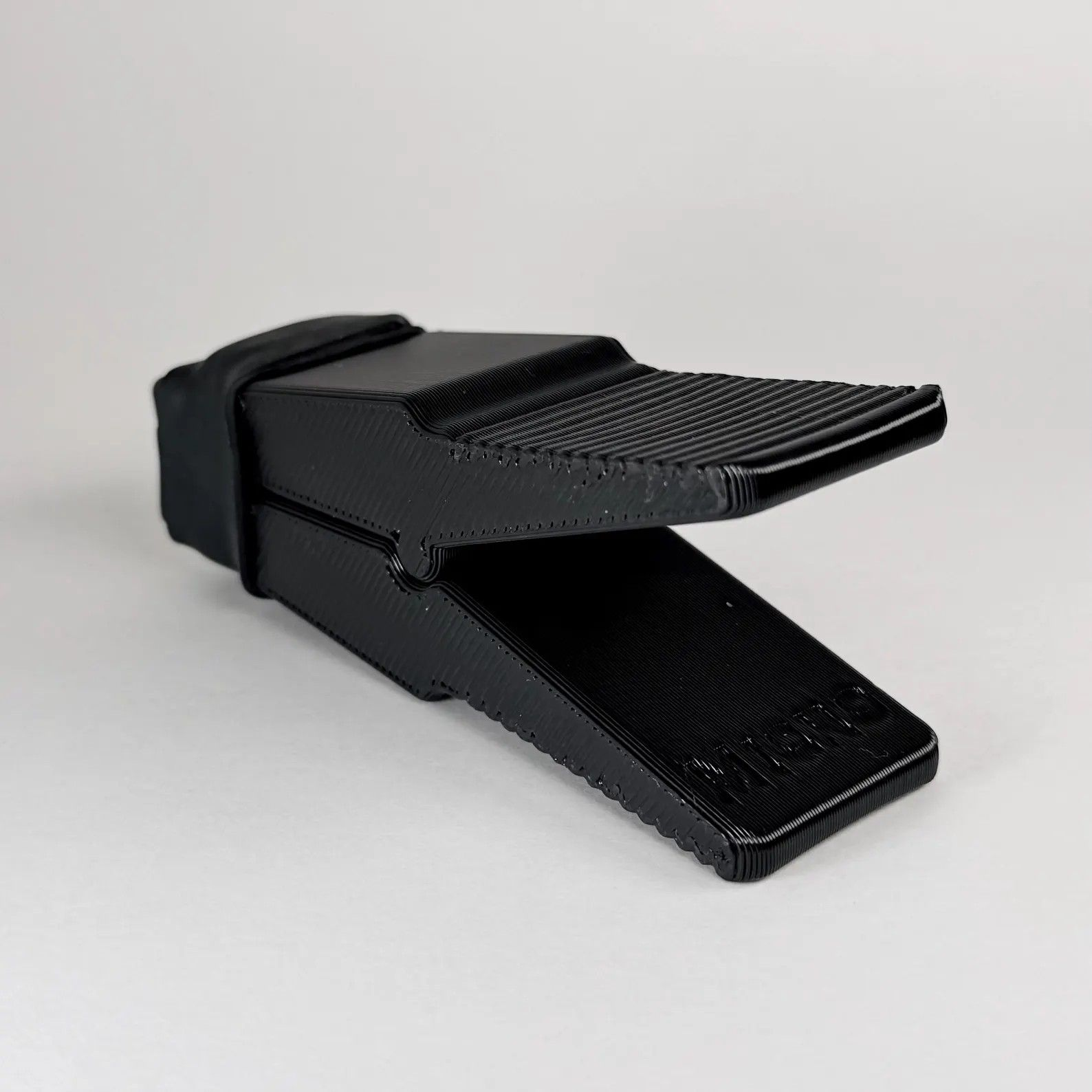A black plastic door wedge stopper featuring a textured top grip surface, viewed from a slightly high angle.