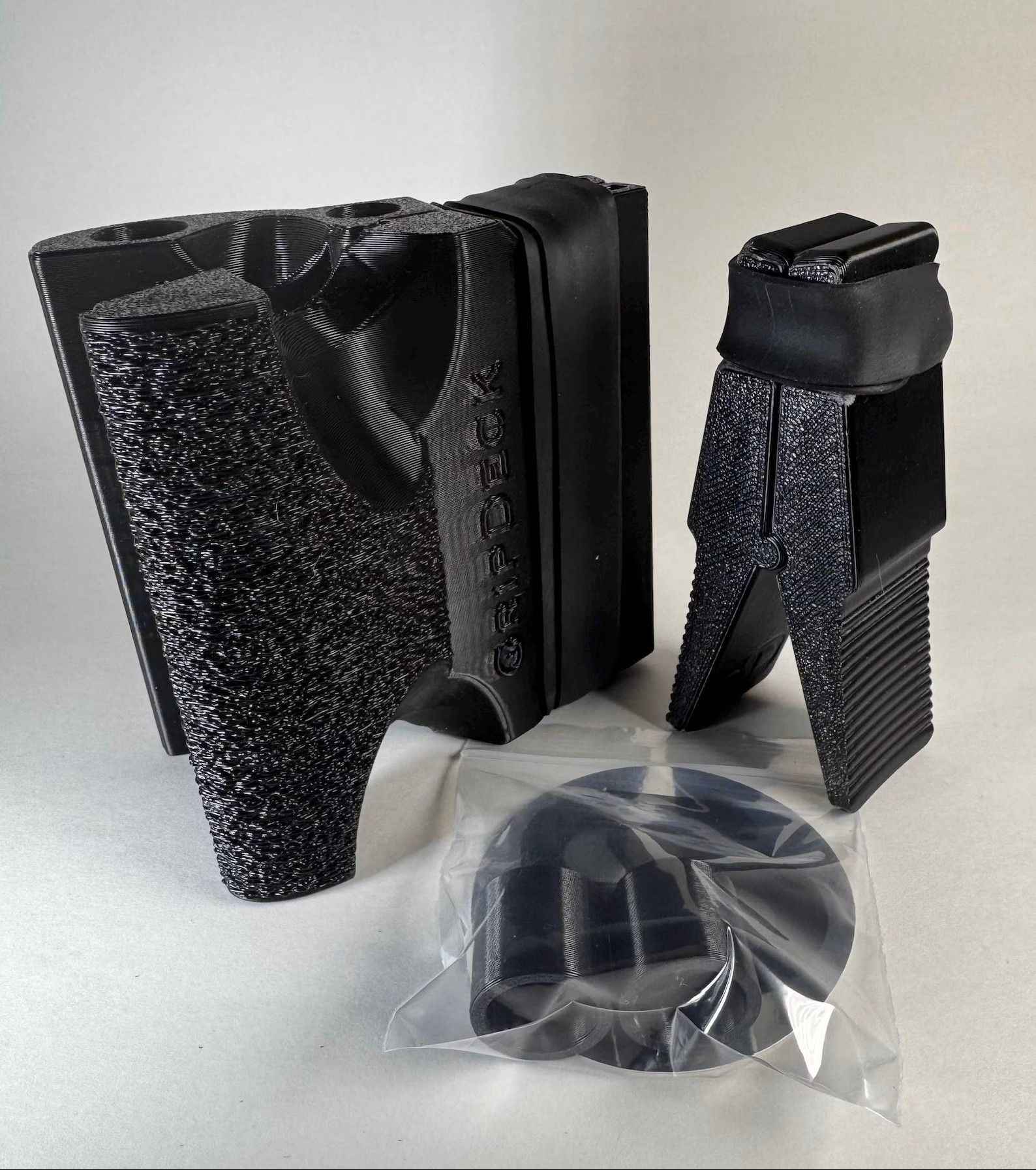 Black, textured, V-shaped athletic equipment components and a circular part in a plastic bag on a white background.