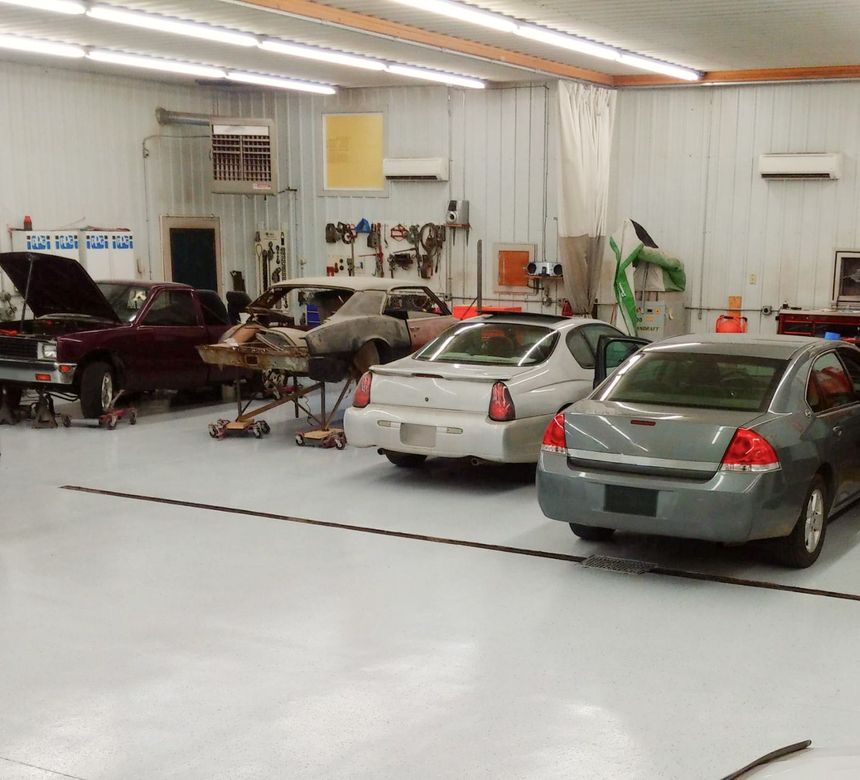 Cars in various states of repair inside a well-lit auto repair shop | Dean's Auto Body