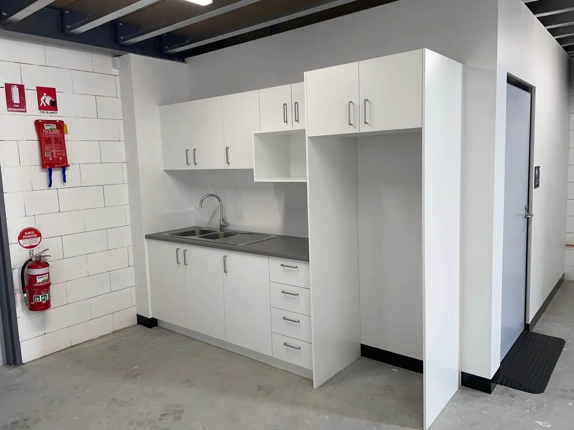 White Kitchenette With Cabinets, Sink, and Refrigerator in an Industrial Space — ATH Projects in Kirrawee, NSW