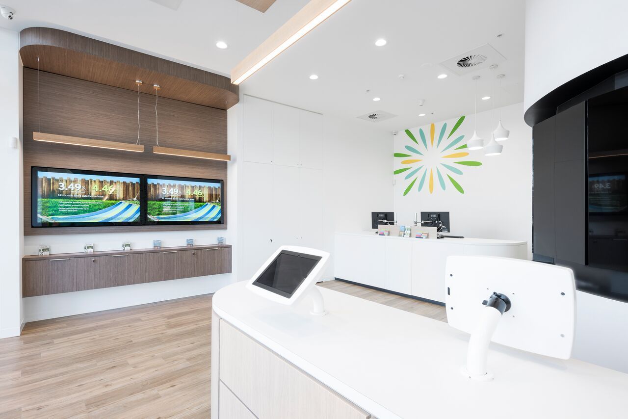 Modern bank interior with a curved white counter, two screens, and a sun-shaped logo on the wall — ATH Projects in Kirrawee, NSW