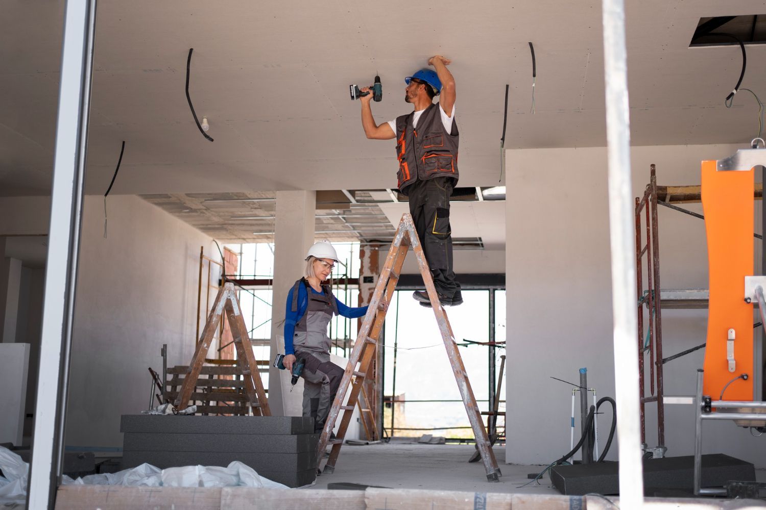 Two construction workers are working on the ceiling of a building.