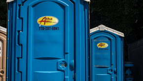 Three blue portable toilets are lined up next to each other.