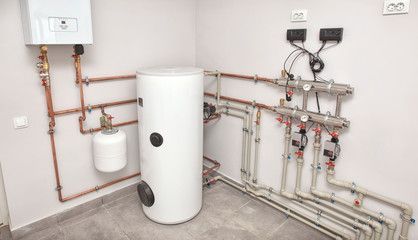 A room with a water heater and pipes on the wall.