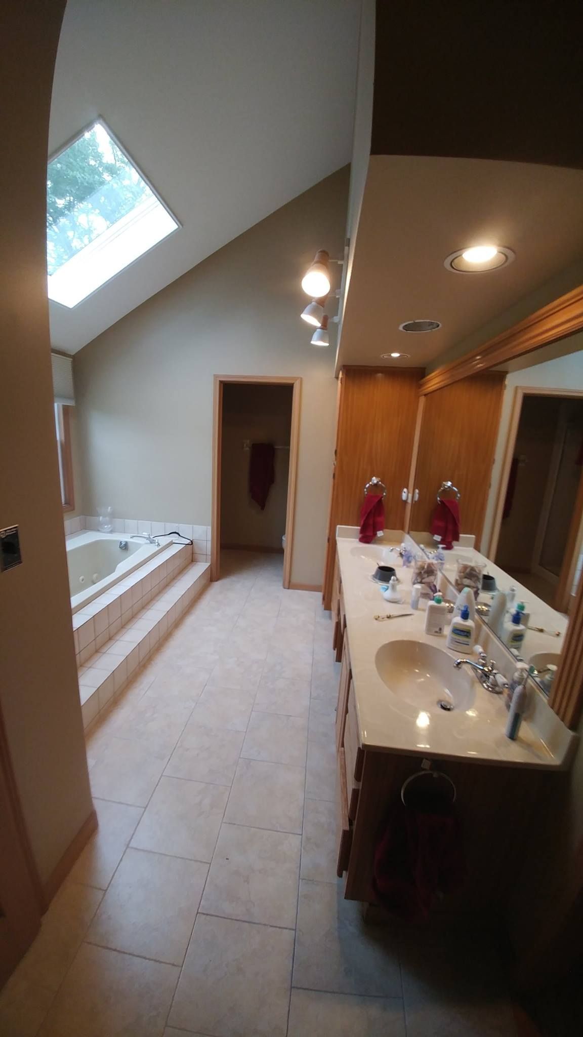 A bathroom with two sinks , a tub and a skylight.