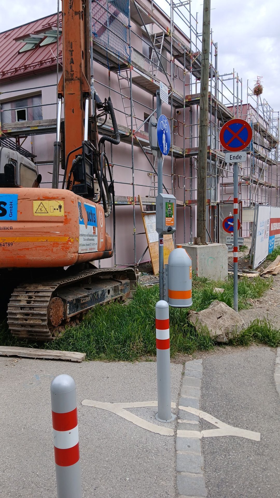 Baustelle mit einem orangefarbenen Bagger und einem Baugerüst an einem Gebäude