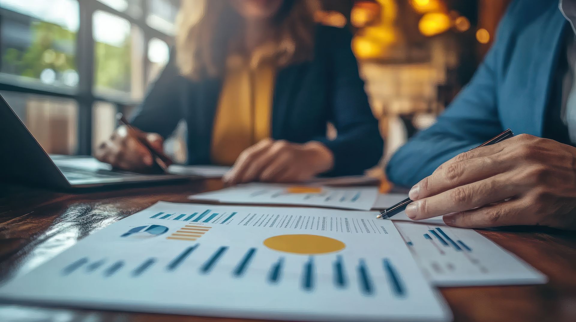 Zwei Fachleute sichten Datendiagramme und Dokumente an einem Schreibtisch in einem gut beleuchteten Büro.