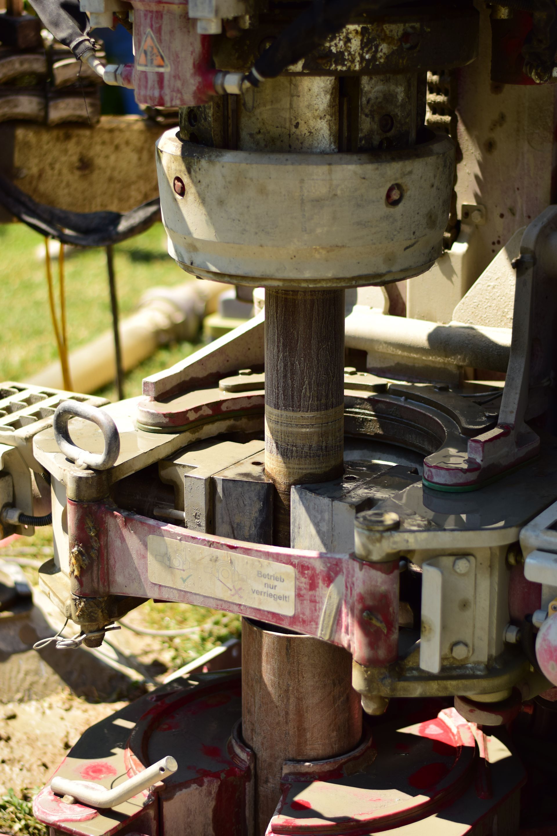 Nahaufnahme einer hydraulischen Bohranlage, die ein mit Eisenklemmen befestigtes Bohrgestänge auf einer Baustelle zeigt.