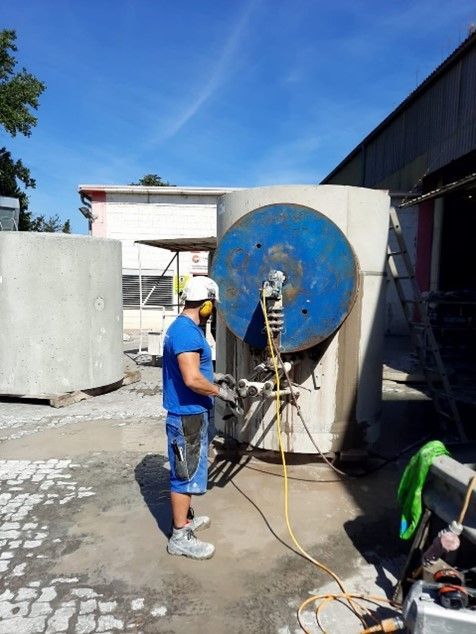 Eine Person in Schutzausrüstung arbeitet an einem großen Betonzylinder mit blauer runder Kappe auf einer Baustelle im Freien.