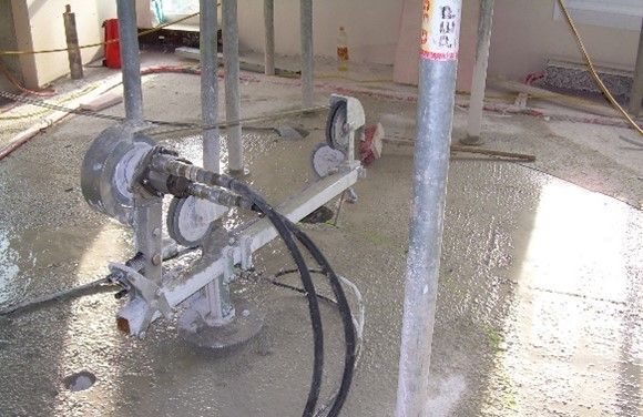 Auf einem nassen, hellgrauen Betonboden einer Baustelle steht eine Kreissägemaschine für Beton.