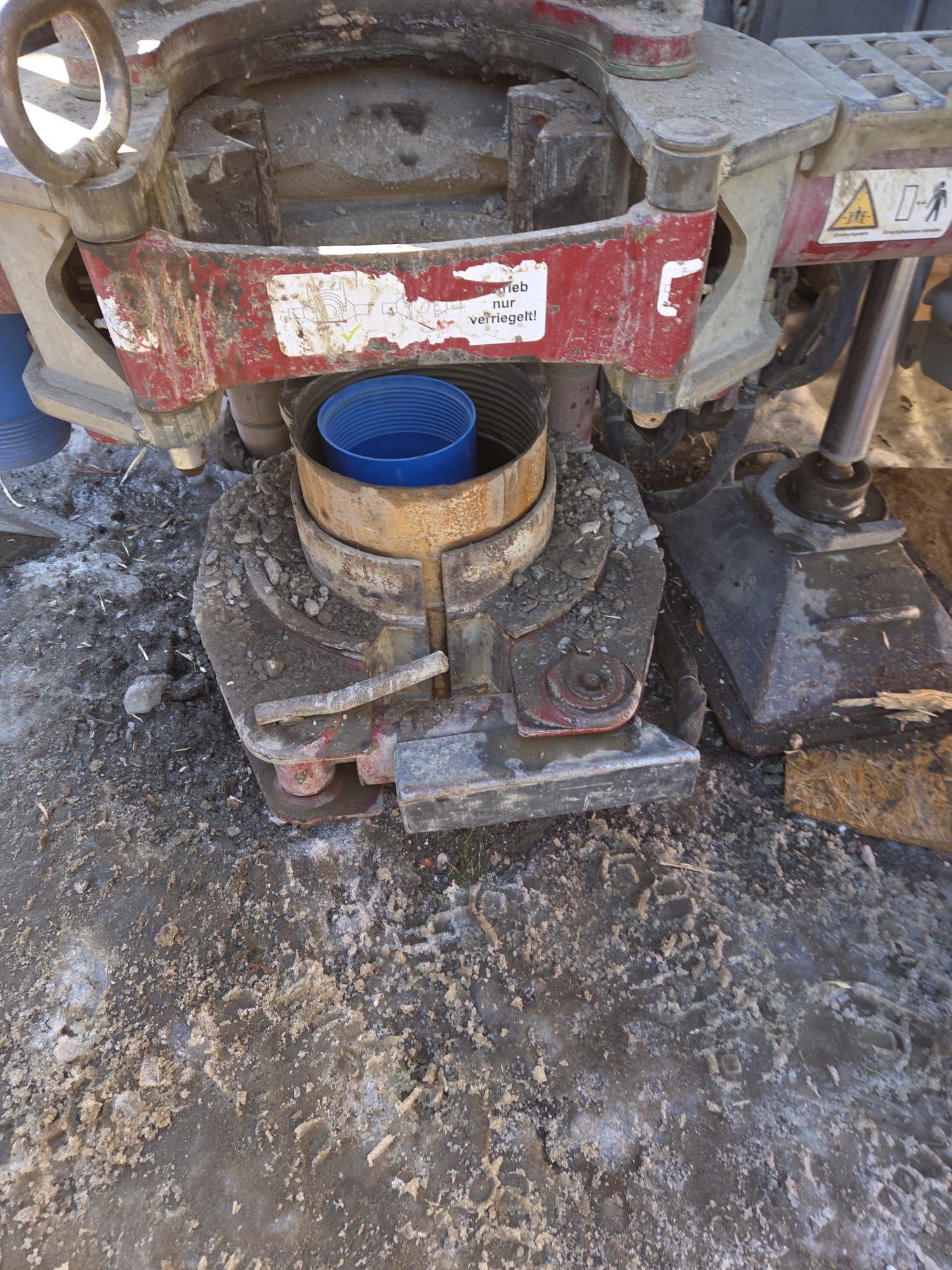Ein drehbarer Metalltisch einer Bohranlage, der ein blaues Rohrsegment über einer schlammigen, ebenerdigen Baustelle hält.