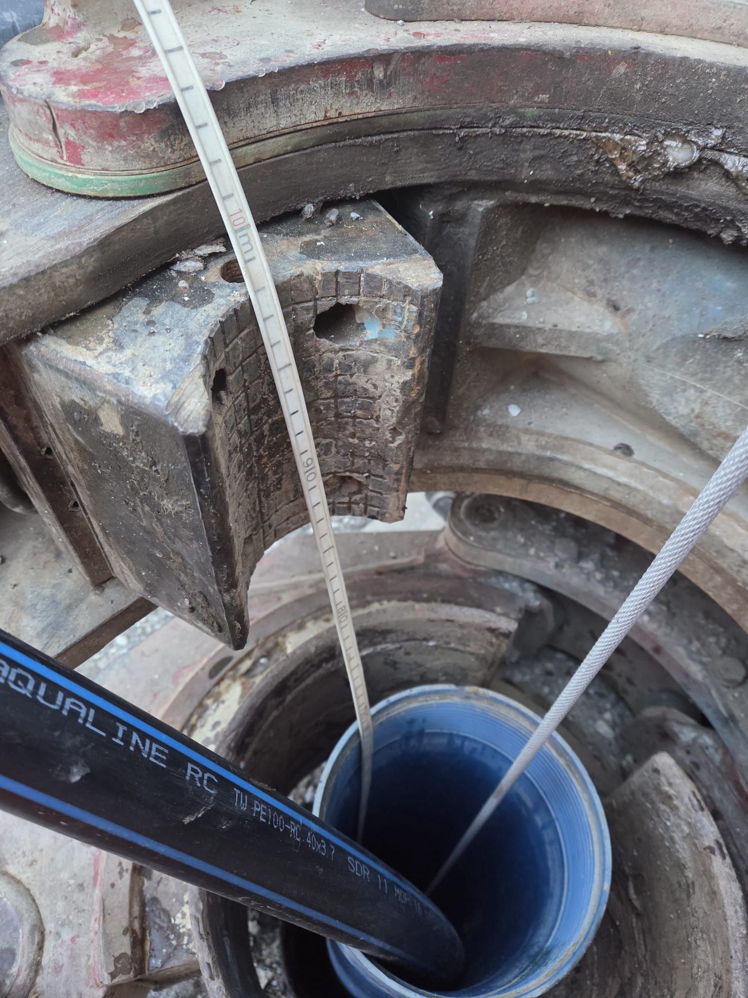 Ein Blick in einen Schacht oder Brunnen mit einem schwarzen Rohr und dünnen grauen Kabeln, die in eine runde Öffnung führen.