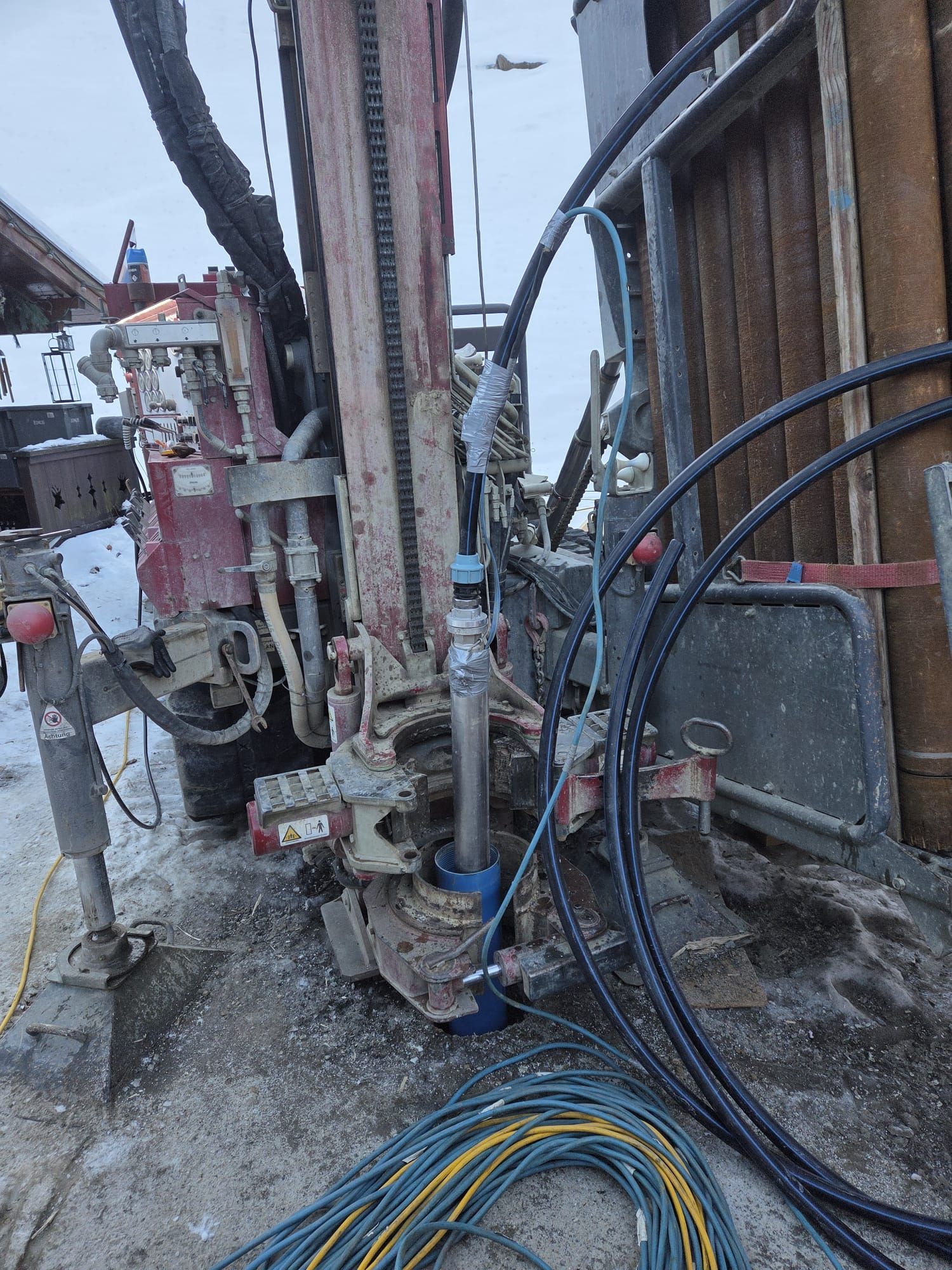 aufgebaute Bohranlage, um die herum Hydraulikschläuche und Maschinenteile sichtbar sind, die sich um den Bohrkopf befinden.