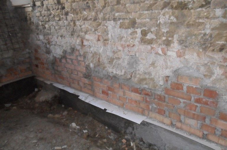 Eine unfertige Innenwand mit Steinmauerwerk oben, roten Ziegeln in der Mitte und einer Schicht aus Feuchtigkeitssperre unten.