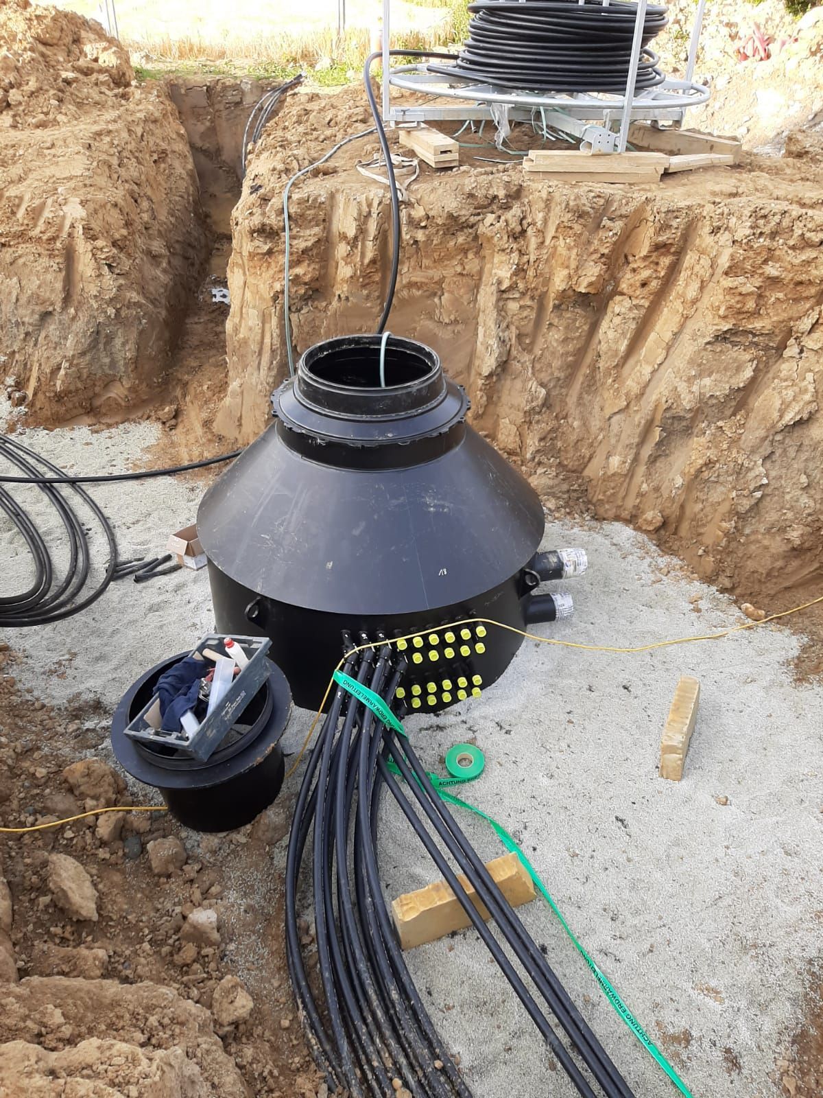 Schwarzer unterirdischer Verteilerkasten, der in einem Erdgraben installiert ist 