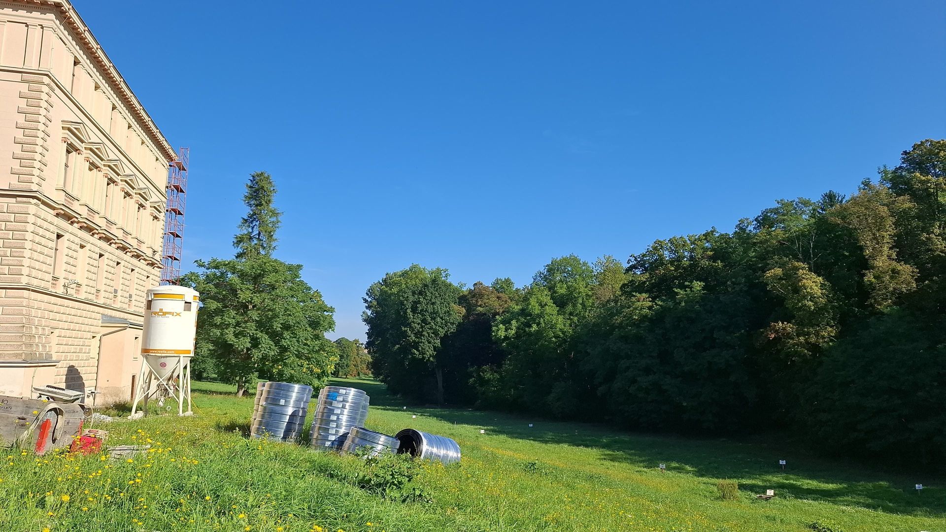Eine Baustelle neben einem Feld mit Bäumen und klarem, blauem Himmel.