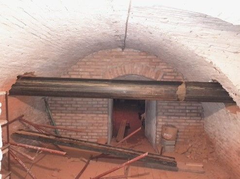 Eine unterirdische, gewölbte Kammer mit Ziegelwänden, in deren Inneren ein Gerüst aufgebaut sind.