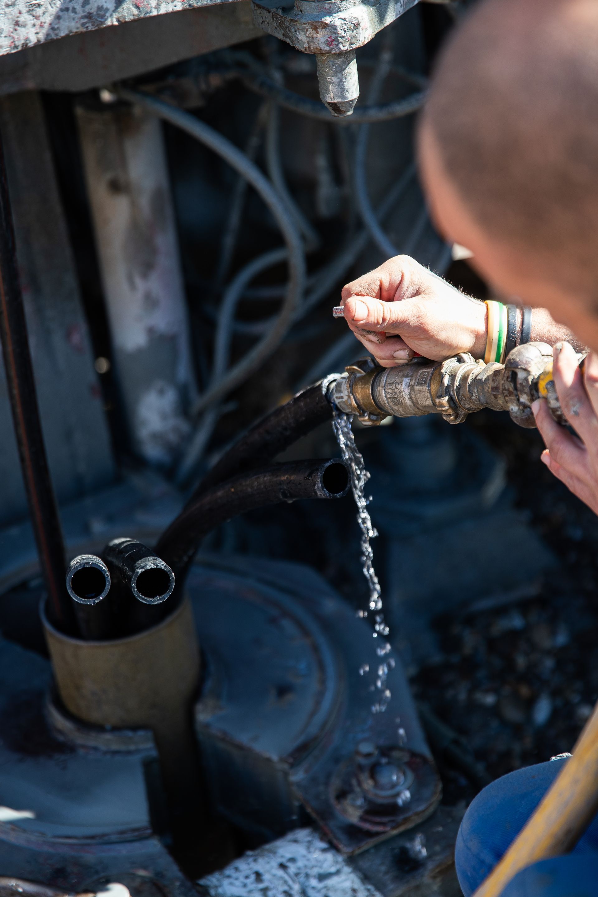 Eine Person hält im Freien eine undichte Rohrverbindung, aus deren Metallgelenk Wasser tropft.