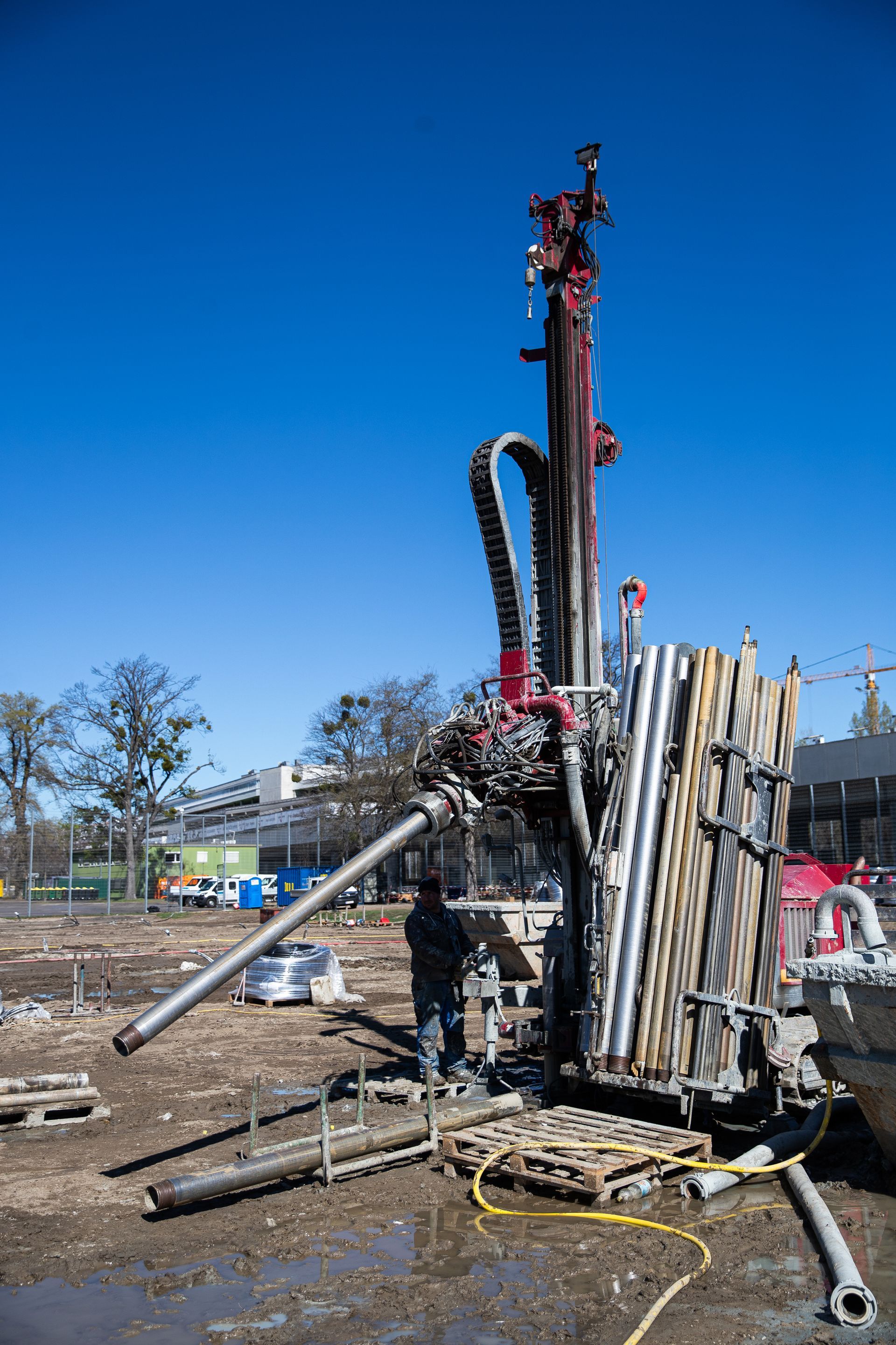 Eine Person bedient ein Bohrgerät auf einer schlammigen Baustelle unter strahlend blauem Himmel.