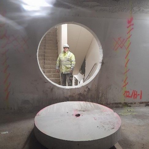 Ein Arbeiter steht hinter einem großen kreisrunden Loch in einer Betonwand, darunter liegt der herausgeschnittene Bohrkern.