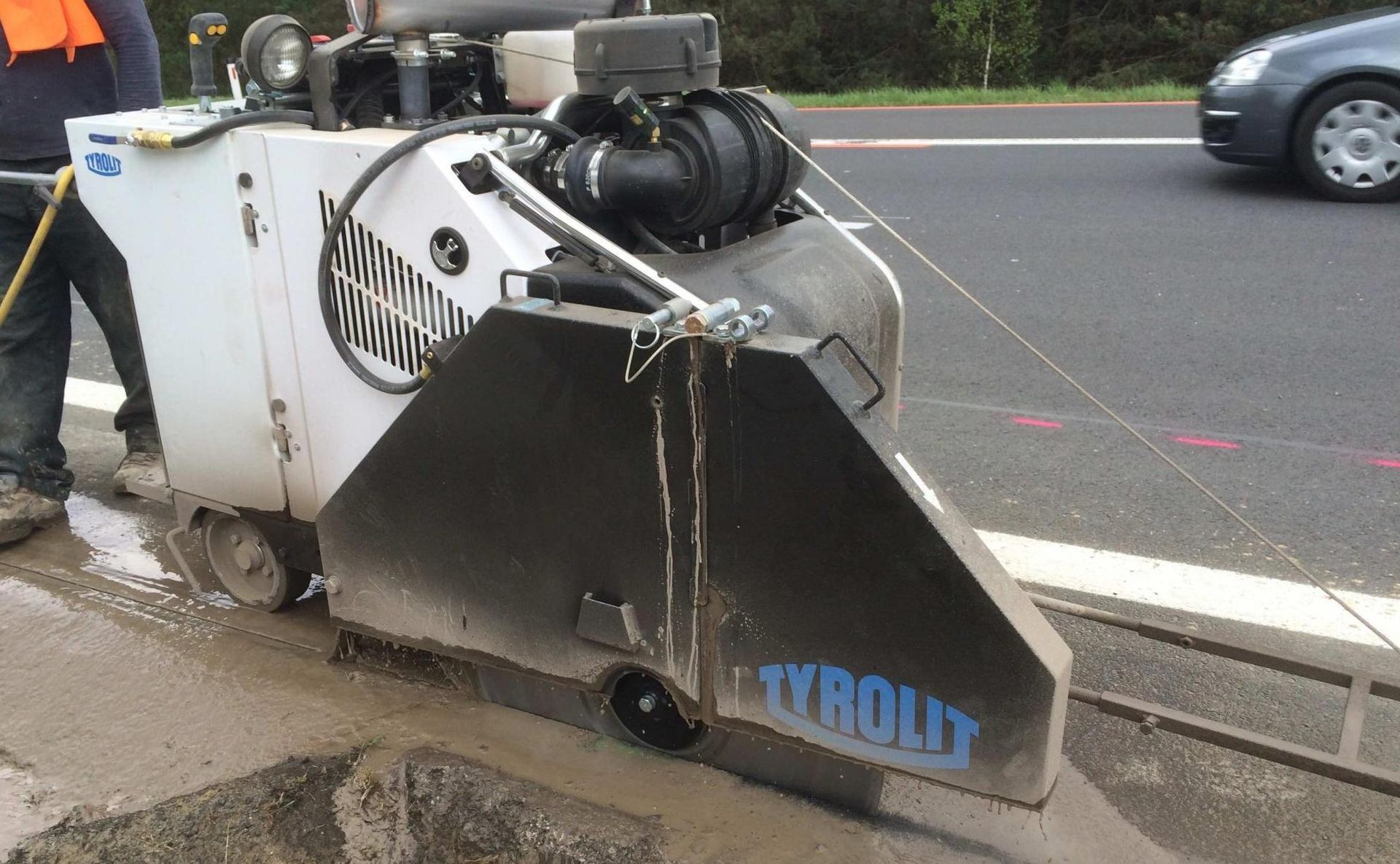 Ein Arbeiter bedient eine große, weiße Tyrolit-Betonsäge, um eine Nut in die Fahrbahnoberfläche zu schneiden.