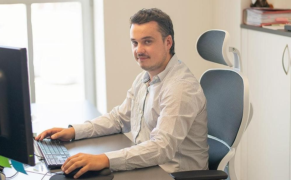 Eine Person in einem gemusterten Hemd sitzt an einem Schreibtisch in einem Büro