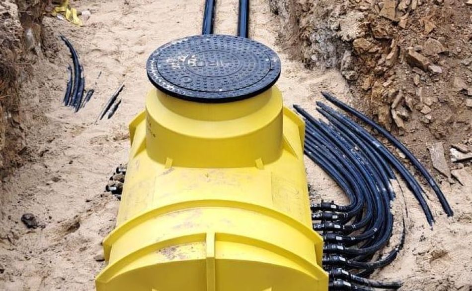 In einem Erdgraben befindet sich ein leuchtend gelber unterirdischer Verteilerkasten