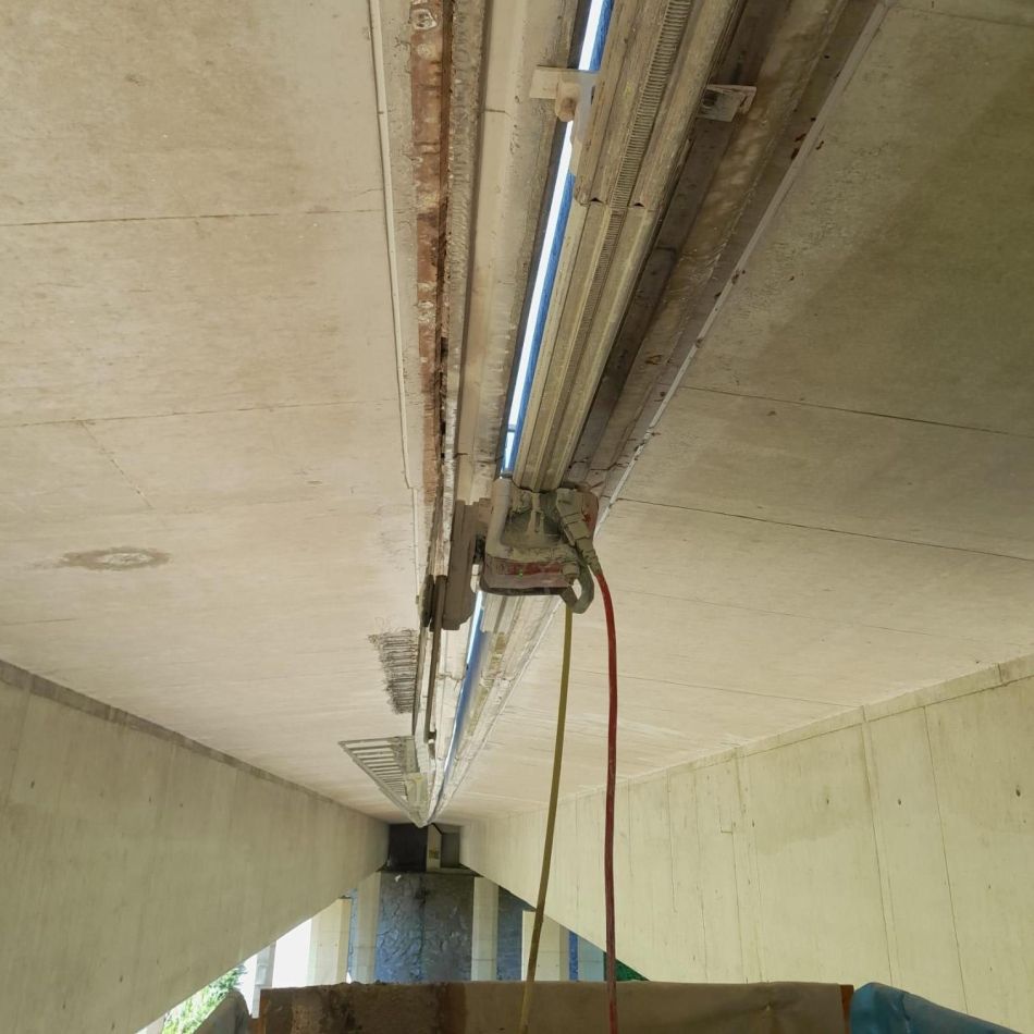 Ein Metallwagen fährt entlang einer Dehnungsfugenschiene einer Brücke;