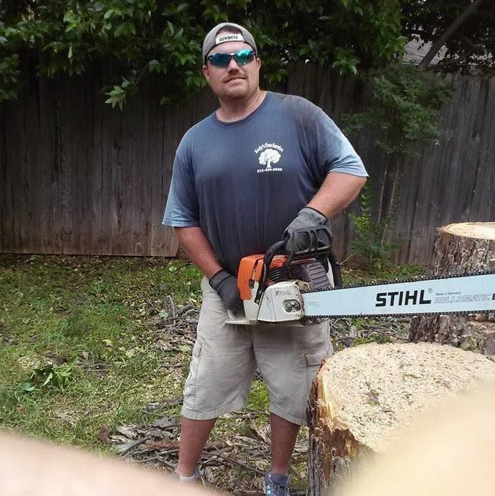 Man holding a STIHL chainsaw beside a cut tree stump in a backyard.