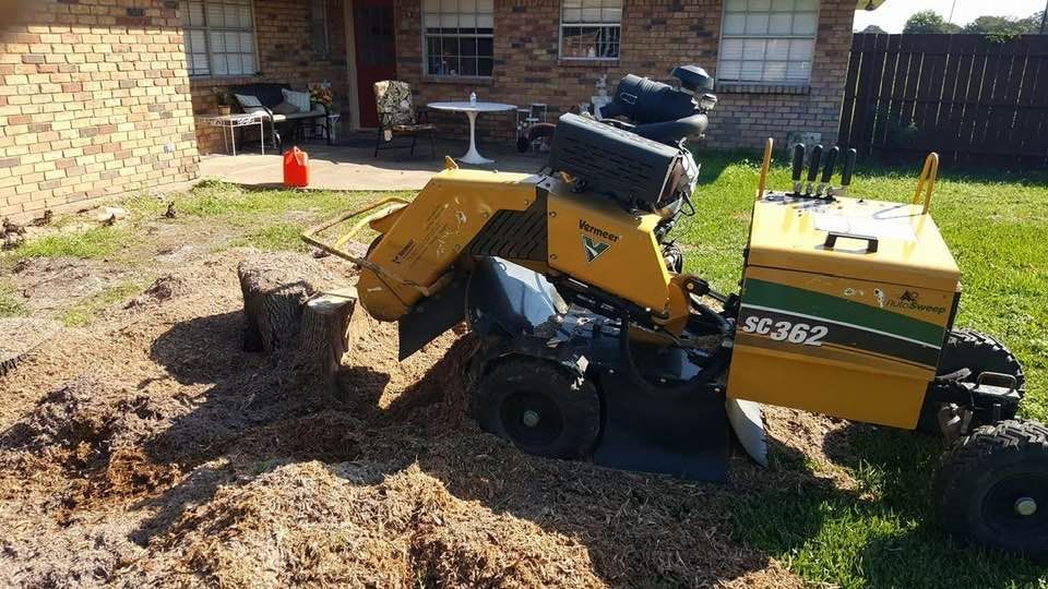 Yellow skid steer loader moving mulch in a backyard beside a brick house
