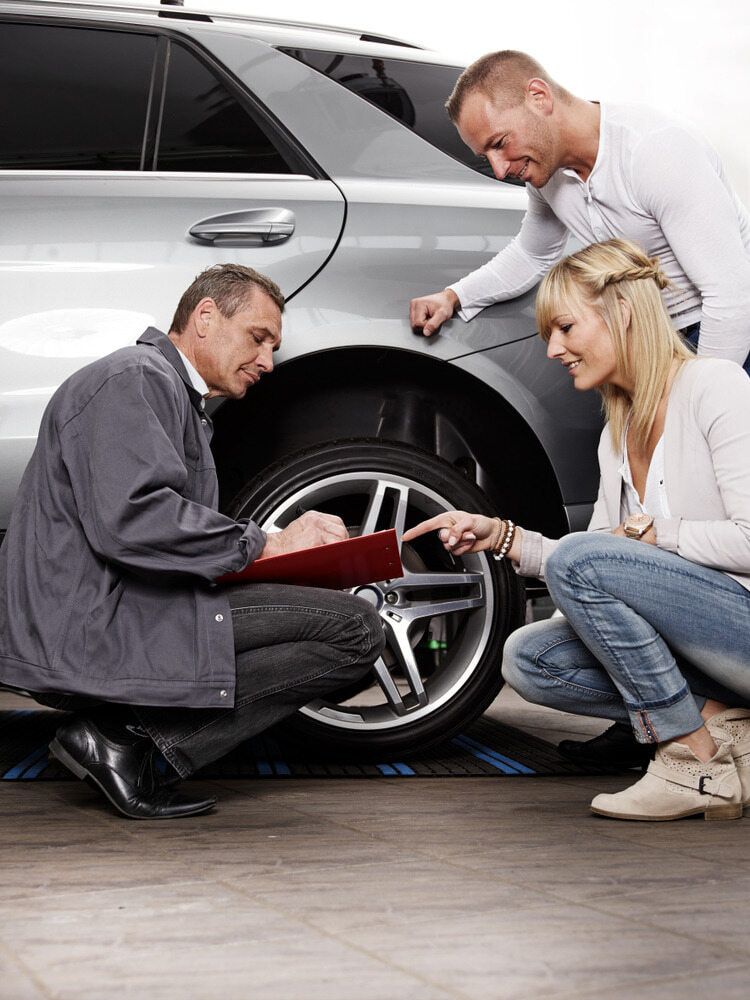 A Man And A Woman Are Looking At A Tire On A Car — Carite Auto Repairs In Warana, QLD