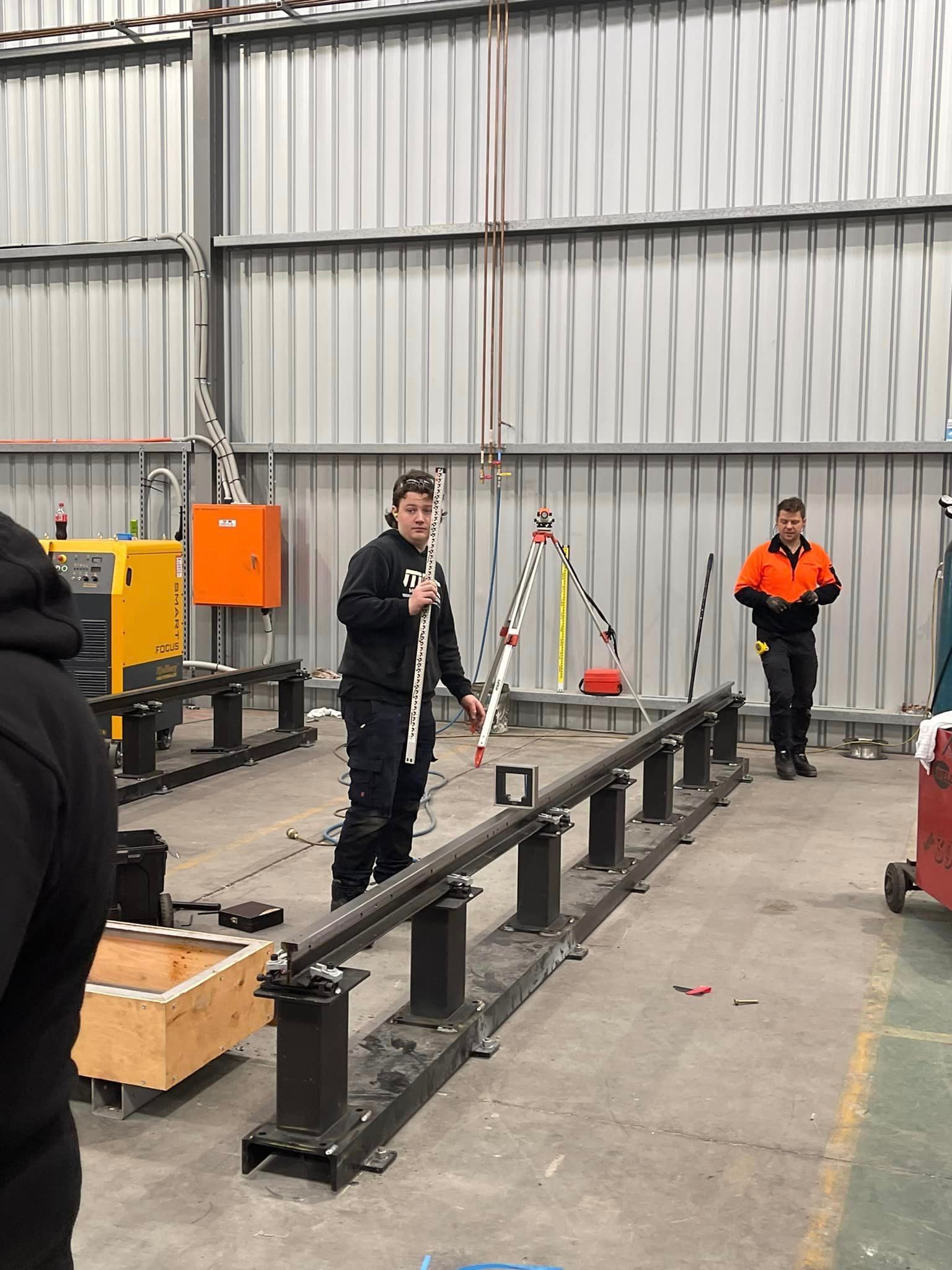 A Man Is Standing On A Railing In A Warehouse Holding A Pole – Wacol, QLD - Morgan Metal Corp