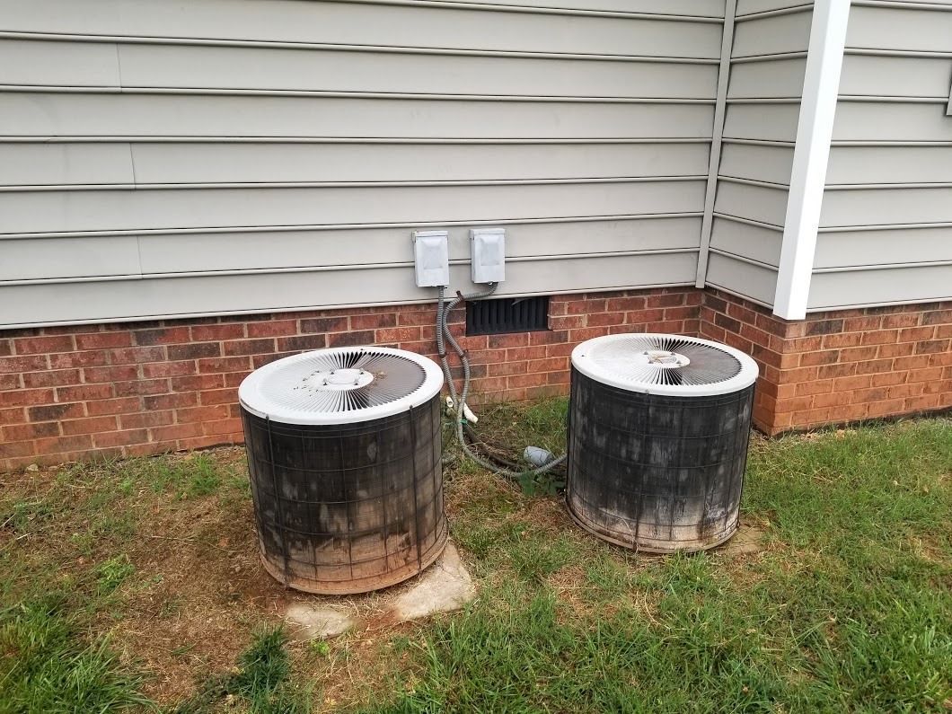 two air conditioners are sitting in the grass in front of a house .