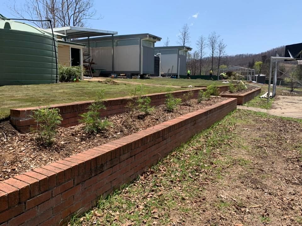 Brick Garden Bed With Small Plants in Front of Buildings — Manning Valley Landscapes in Forster, NSW