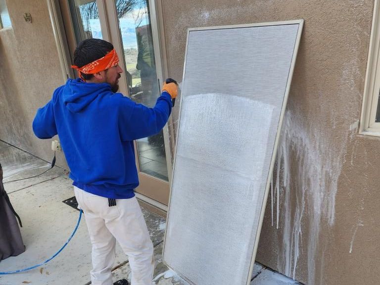 A man in a blue hoodie is cleaning a window screen.