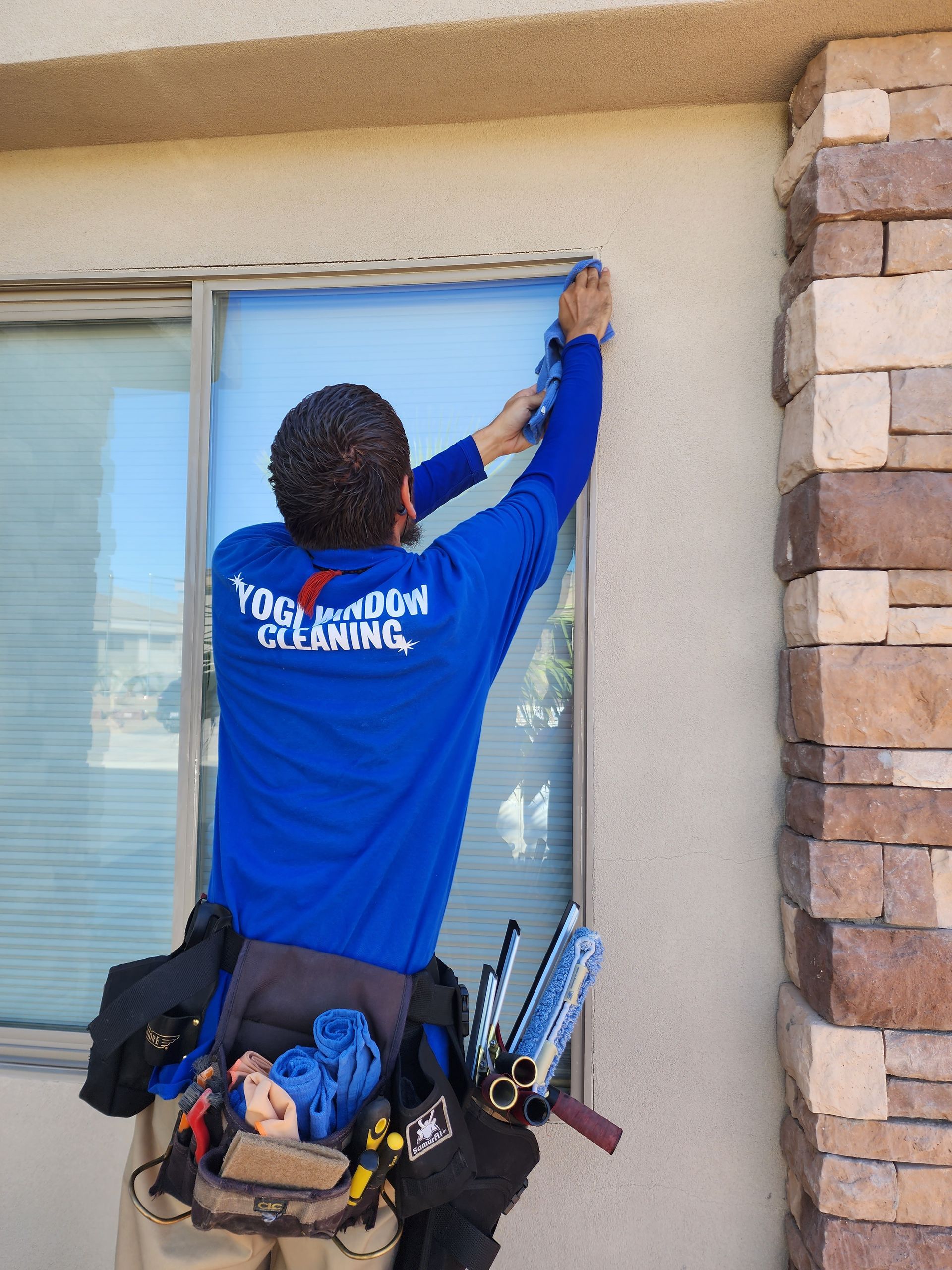 A man wearing a blue shirt that says tong room cleaning is cleaning a window