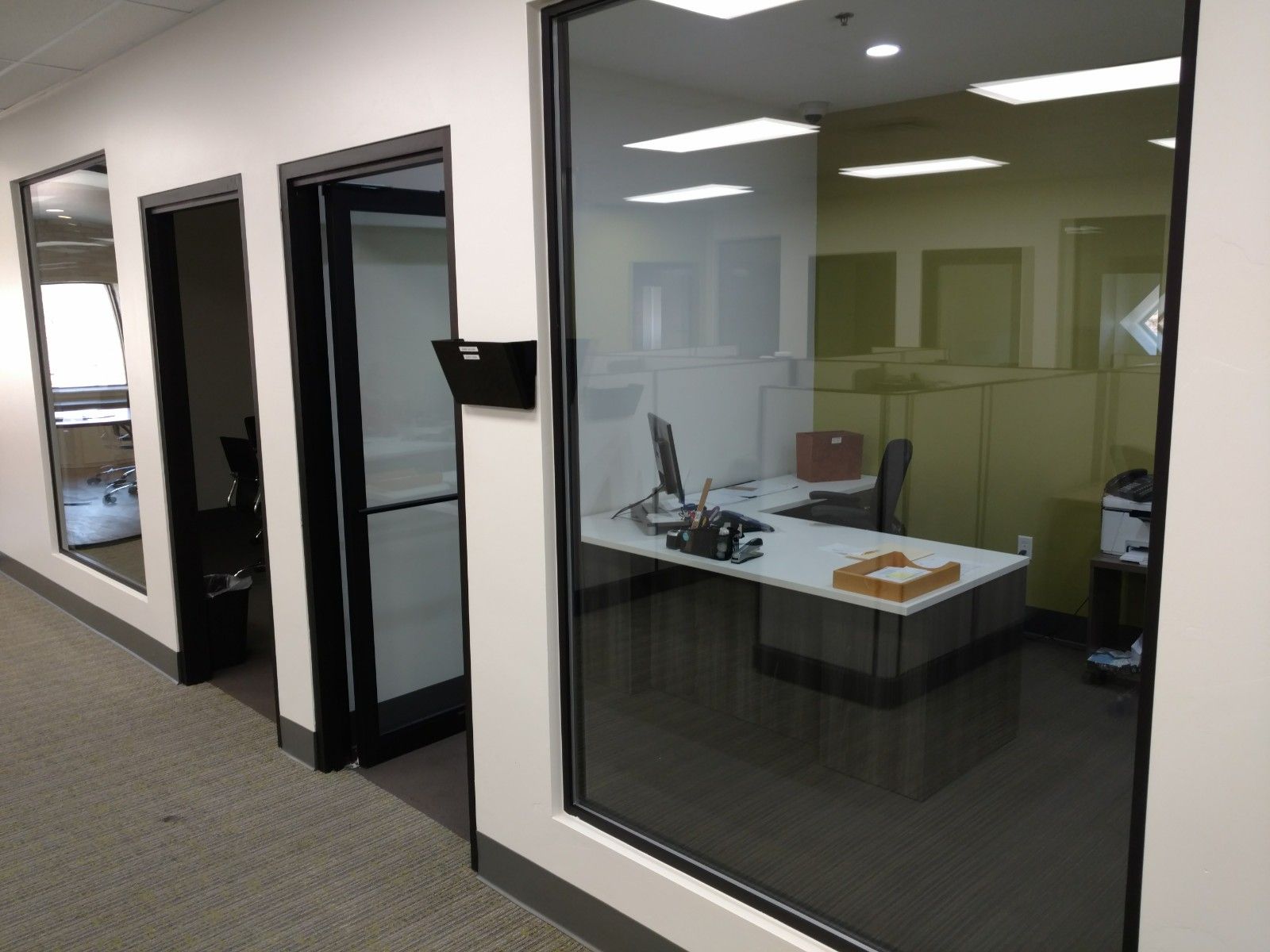 A hallway with cubicles and a desk with a computer on it.