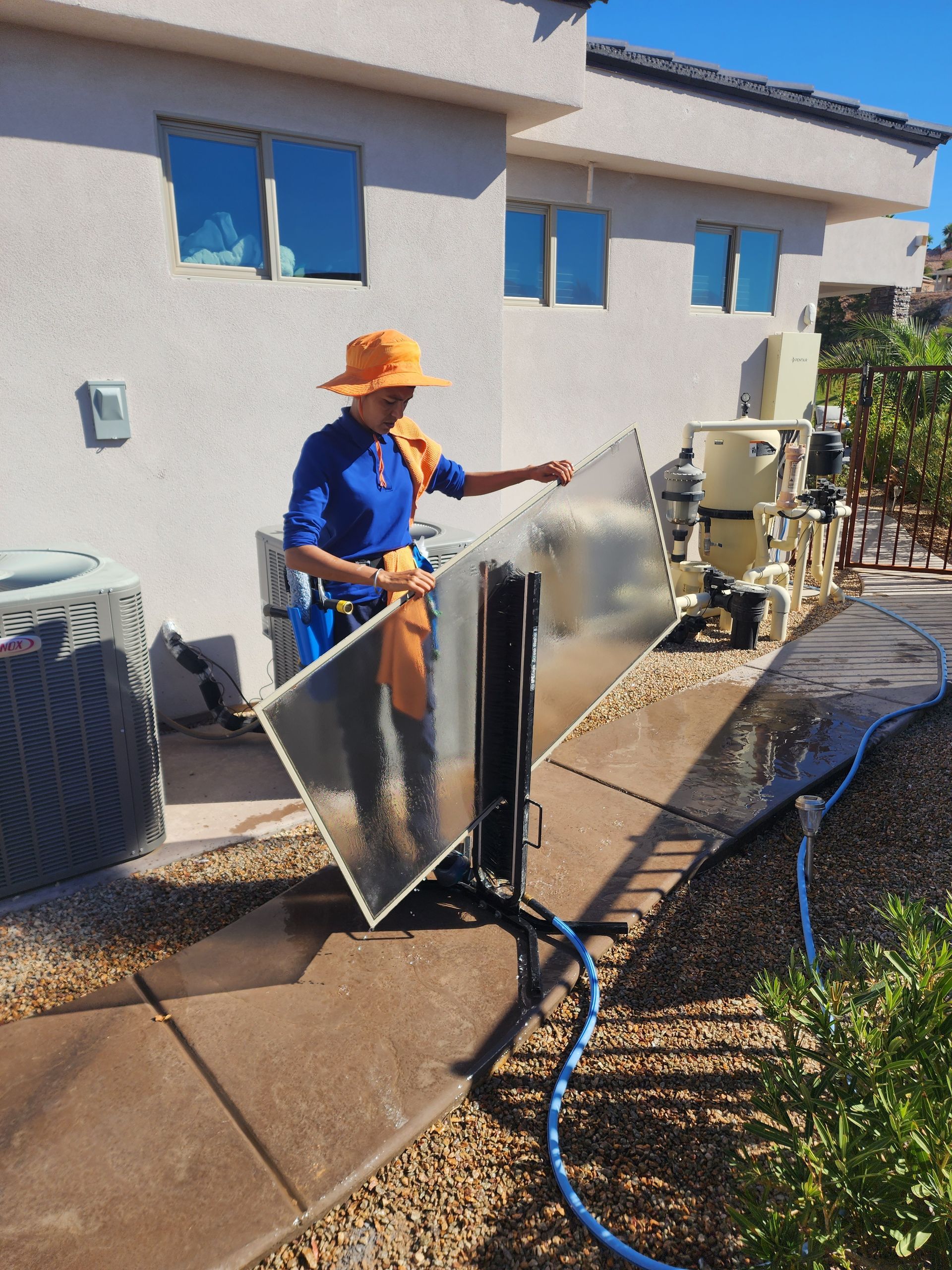 A man in an orange hat is cleaning a window with a hose